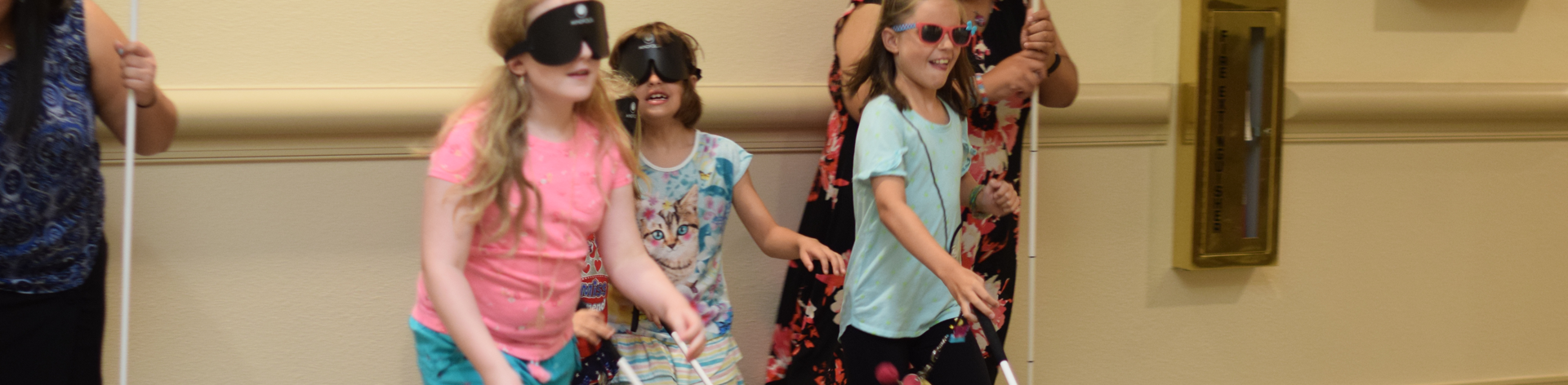 Four young blind girls smile under sleepshades as they run a race using thier long white canes.